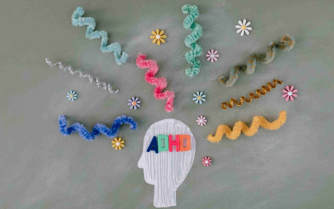 A painted head surrounded by squiggly pipe cleaners and flower stickers with the letters ADHD over the head in magnetic letters