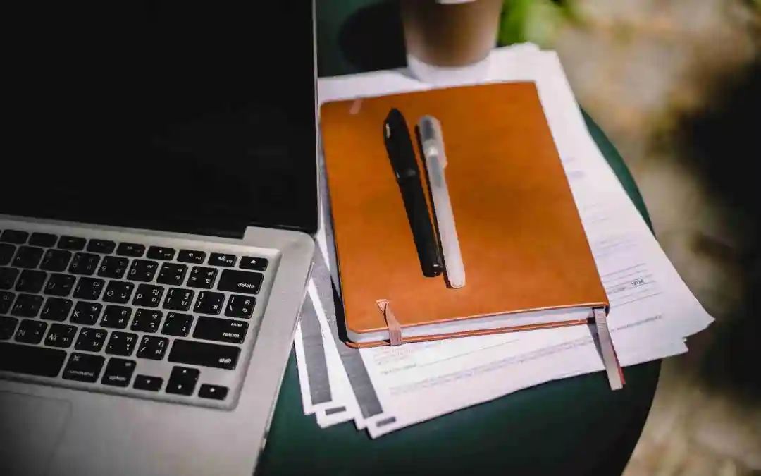 black and white pens on a journal on papers next to a computer